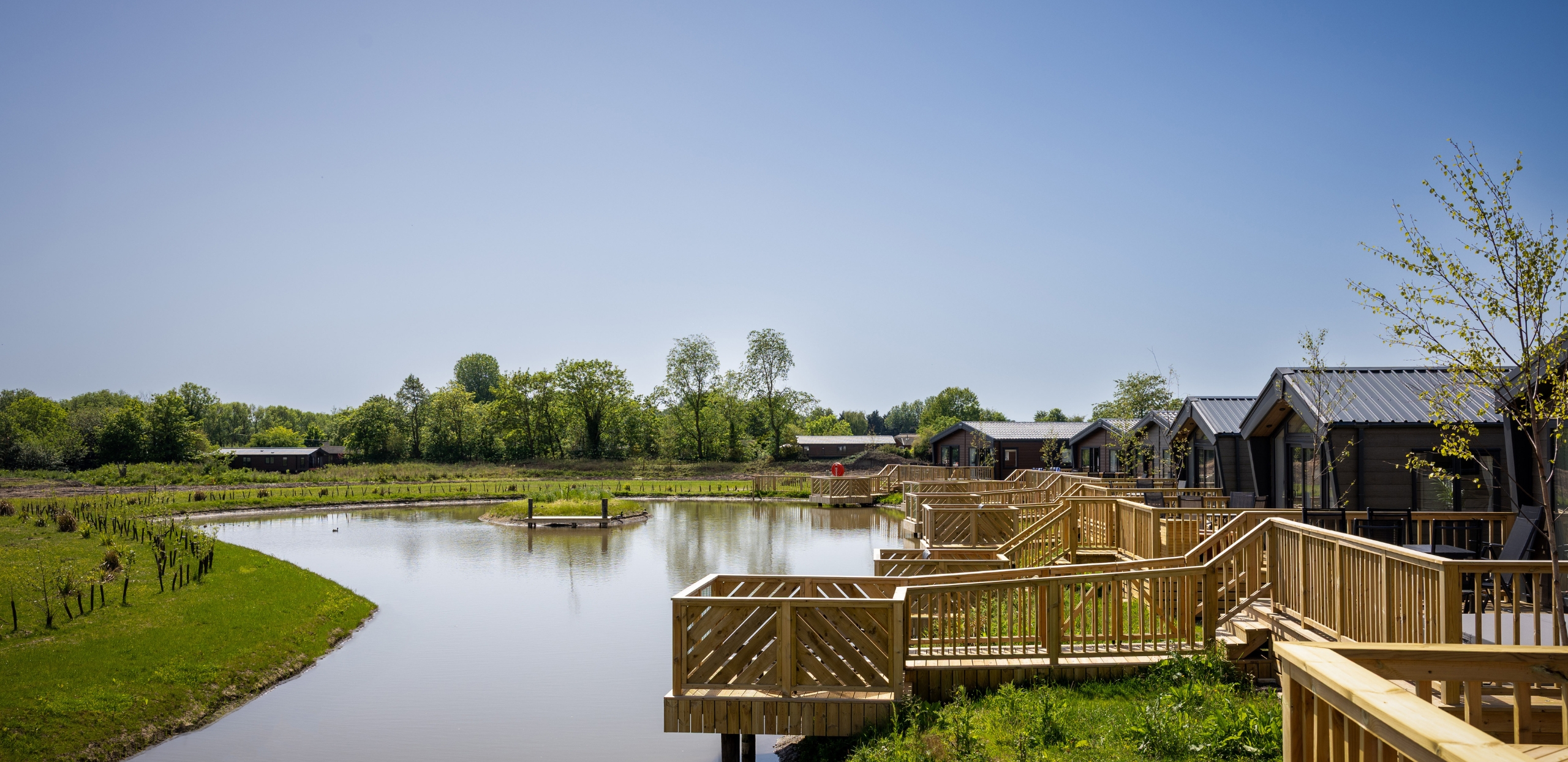 A lake surrounded by wooden decking from a selection of luxury lodges along one edge
